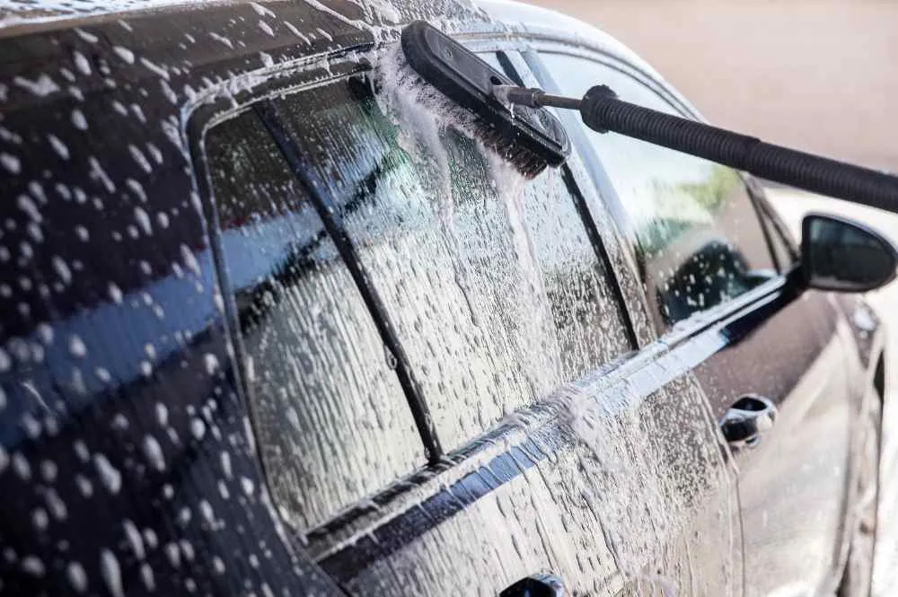 a man using a brush on black car and guiding how to wash car properly