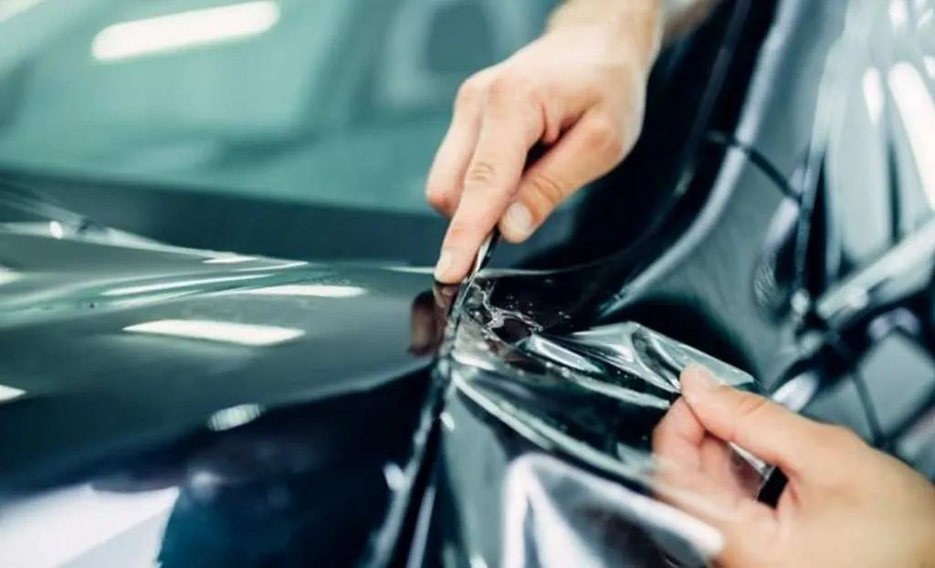 hands applying the paint protection film on a black car